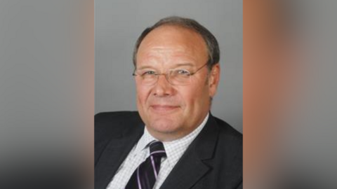 Stuart Munro's official councillor photo, with him dressed in a suit looking at the camera. He has short, grey hair and is wearing glasses.