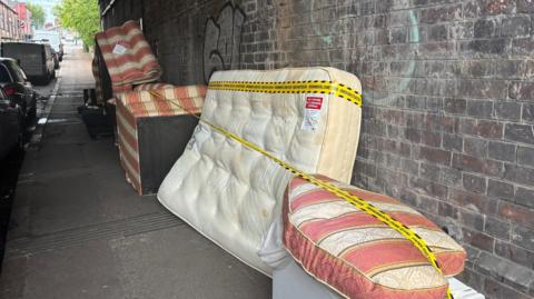 Taped off furniture on the side of a road beneath a bridge