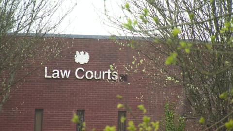 The outside of Bodmin magistrates court. The words Law Courts are displayed in silver on a solid brick wall. There are trees and branches in front of the building. 