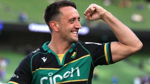 Northampton Saints' Alex Mitchell smiling and raising a fist next to his head with his left arm bent 