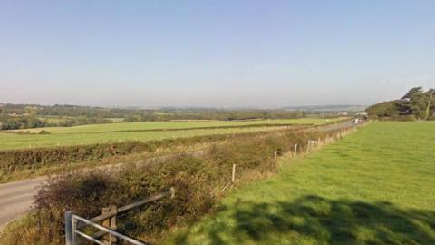A Google Street View of Briddlesford Road, a country road that lies between fields.