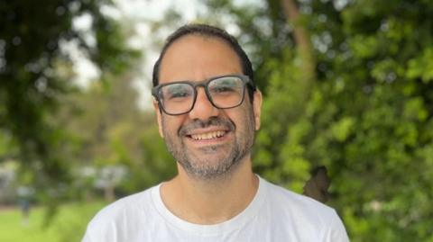 Alaa Abdel Fattah dressed in a white T-shirt and wearing black rimmed glasses.