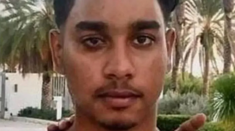 A close up of Shawn Seesahai's face. He is standing in front of palm trees and a white wall