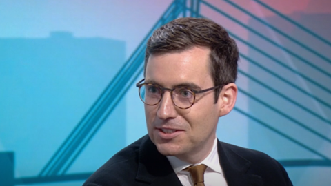 Dan Price, wearing a black suit, white shirt and brown tie, talks in the BBC's Salford studio.