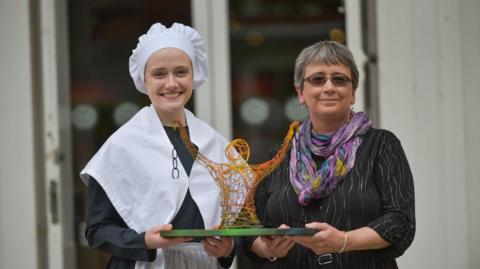 Two women holding a gold statue with chains from each hand