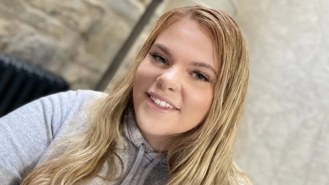 Bethany Branson smiling at the camera. She has long blonde hair, a piercing in her nose and is wearing a light grey hoodie. 