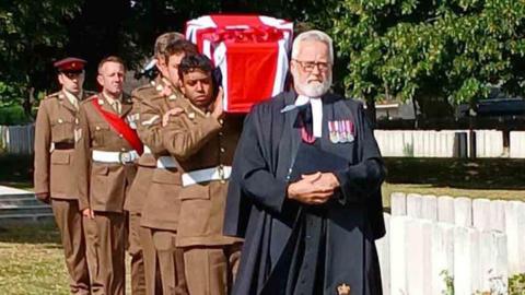 A coffin covered in a British flag being carried by soldiers.