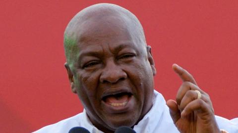 Ghanaian President John Dramani Mahama speaks at a press conference, with a red backgroud behind him