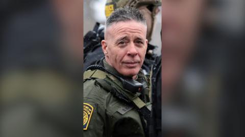 A man, border patrol commander Greg Bovino, in uniform looking at the camera.