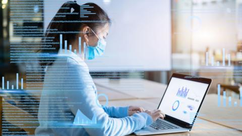 Businesswoman with protective face mask works on virtual visual screen in office.
