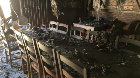 A table which is covered in ash, below the roof which has debris hanging off it. 
