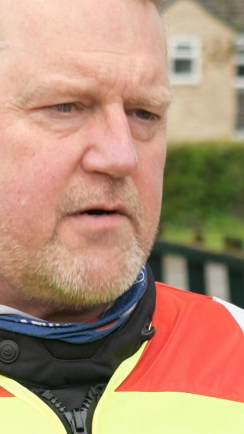 A man with a beard and bright-coloured motorcycle leathers on faces the camera