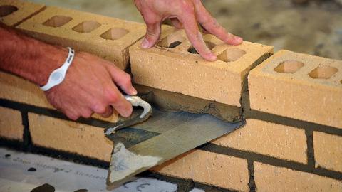 Close up of a man's hands holding a trowel and brick as he builds a brick wall