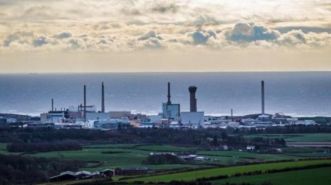 General view of Sellafield Nuclear power plant, in Cumbria. The shot is taken from a distance further away, with the sea on the horizon and a cloudy, but sunny day. The forefront is green areas of land.