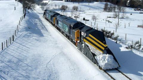 A Network Rail train sweeping snow out of the track in a snowy field 