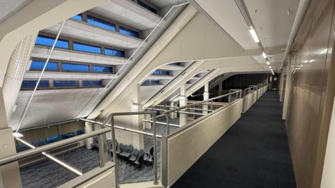 View from the first floor of Carlisle Library looking onto the floor below. It is an open plan area, with new navy carpets and lots of office chairs lined up on the ground floor. 
