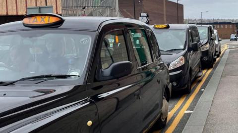 A row of black cabs waiting on double yellow lines