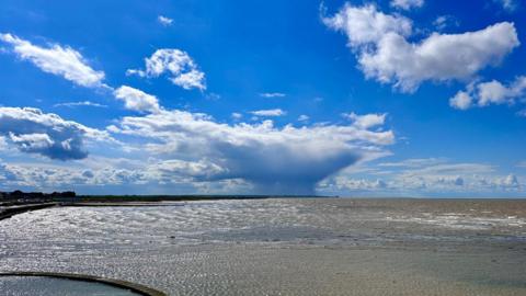 The sun sparkles off the water with large white clouds in a blue sky