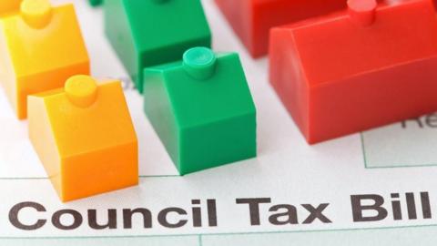 A council tax bill with Monopoly-style houses on top of it - two yellow, two green and two red