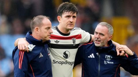 Harry Maguire is helped from the field by two members of Manchester United staff