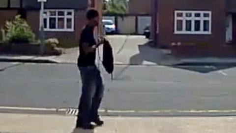 A man in dark clothes seen from side view walking along a residential street in partly blurry CCTV or doorbell footage 