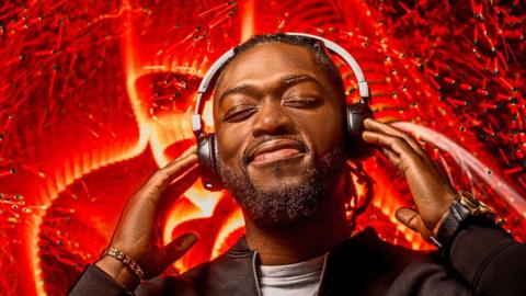 A man wearing headphones with red lighting effects behind him