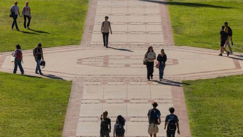 Students, a number in backpacks, walk solo and in pairs on the grounds of college campus