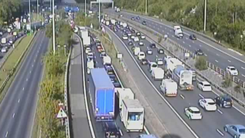 A motorway traffic camera image showing queueing cars, vans and lorries on the M60.