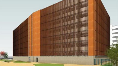 A digital image of a large mostly brown building, it is six stories high. Around the building are open spaces with some trees.