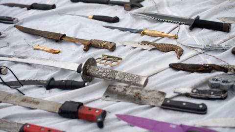A selection of different knives laid out on a blanket, with different coloured handles and blades.