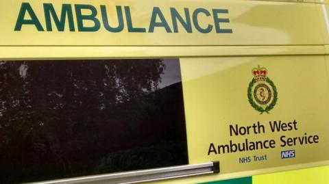 A close-up of a yellow ambulance with green writing on the side that reads North West Ambulance Service. 