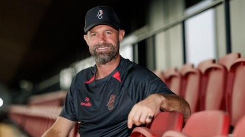 Louis Carey sitting in the stands at Ashton Gate, wearing a Bristol City branded black t-shirt and black cap. 