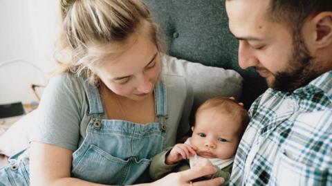 A couple with a baby on a sofa.