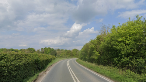 A single carriageway A-road near from Frome which has no cars on it, but has road markings and green grassy verges and bushes.