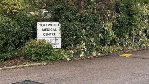 A sign for Toftwood Medical Centre. There are lush green hedges behind it