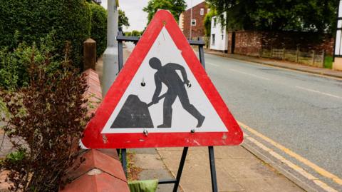 A men at work triangle sign next to a road