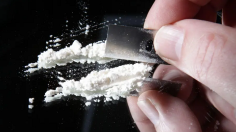 A hand cutting white powder with a blade on a mirrored surface