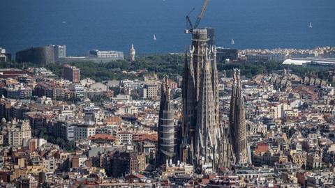 The Sagrada Familia is pictured with a crane perched on top of it's central turret, with the rest of Barcelona stretched out behind the famous church.