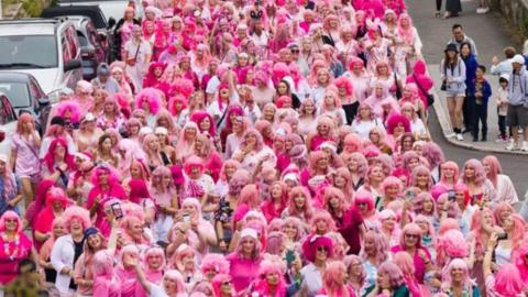 Hundreds of women, wearing pink wigs and pink clothes, parading down the street, cheered on by onlookers