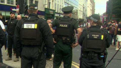 Three police officers with their backs to the cameradges on their uniform