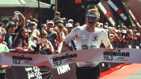 A photo of man wearing sunglasses crossing the finish line of a competition 