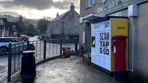 A street corner with a white and yellow parcel locker outside a shop