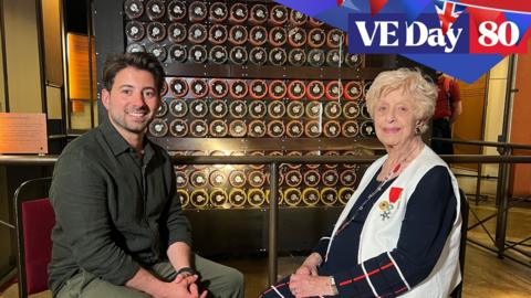 Ricky sits with Ruth Bourne in front of a Bombe machine replica