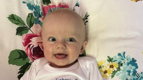 A happy-looking baby lies on a flowery cushion. 