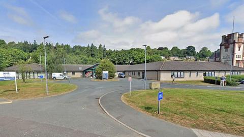 Hawick Community Hospital - a single-storey functional brick building with a car park in front of it and trees in the background