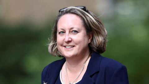 Anne-Marie Trevelyan is walking while looking beyond the camera. She has mid-length brown hair and is wearing a blue blazer.