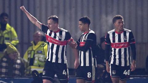 Kieran Green (left) holds his right arm in the air with his fist clenched in celebration of his goal as team-mates stand next to him