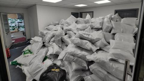 Two large piles of bags, most of them white, are in two adjoining rooms.