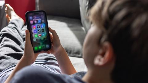 A child lies on a couch holding a smartphone looking at social media apps