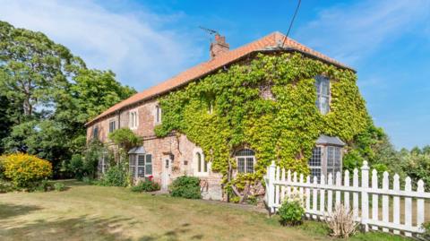 An manor house surrounded by trees with a white fence